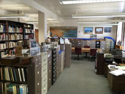 Interior view of a section of the San Pedro Bay Historical Society Archives, showing file cabinets, displayed photos and paintings